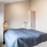 Schlafzimmer mit Bett, blauer Decke und zwei weißen Schränken an den Wänden.