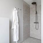 Dusche mit Steinfliesen und Duschbrause. Bademantel hängt an Wand.