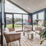 Terrasse mit Rattanmöbeln, Tisch und Pflanze. Durchgehende Glasfront mit Blick auf Parkplatz.
