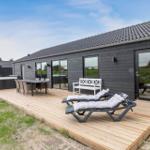 Holzterrasse mit Liegestühlen, Tisch und Whirlpool vor einem modernen Haus.