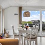 Dining area with view of terrace and sea. White table, chairs, and pendant light.