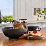 Breakfast with bread, cheese, and tomato on wooden table. Background window with view of greenery and binoculars.