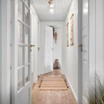 Hallway with white walls, wooden floor, and doorways. Rug and plant are visible.
