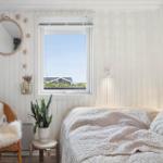 Bedroom with bed, chair, and window view of house and sky.