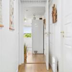 Hallway with white walls, wooden floor, and doors. Pictures and a wooden object hang on the wall.