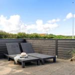 Terrace with two lounge chairs, wooden border, and view of greenery.