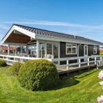 Modern holiday home with terrace and garden. View of the house with wooden veranda and green lawn.
