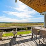 Deck with table and chairs, view of water and grassland.
