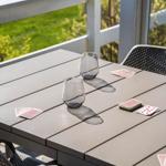 Outdoor table with glasses and playing cards on terrace with view of green area.