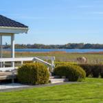 House with terrace and view of a lake with shoreline vegetation.