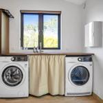 Laundry room with washing machine and dryer under wooden counter with window.