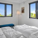 Room with two windows, view of water and greenery, bed with white linens, blue bench.
