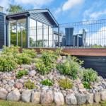 Modern villa with terrace, garden, and stone beds under blue sky.
