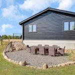 Black wooden house with outdoor seating area. Grassy area and stone walls surround the terrace.