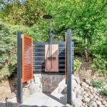 Outdoor shower with wooden door and stone base in green surroundings