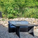 Outdoor area with seating, table, and stone wall. Background: greenery and shower area.
