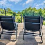 Two black lounge chairs on a wooden terrace with view of green areas and water.