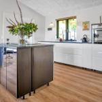 Modern kitchen with island, white cabinets, and wooden floor.