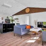 Living area with sofa, table, and TV. Kitchen with countertop and windows.