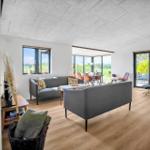 Living and dining area with sofa, table, and windows. Wooden floor and modern furnishings.
