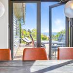 Through the glass doors, you can see a terrace with loungers and a view of the water.