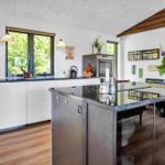 Modern kitchen with island, white cabinets, and wooden floor. Windows with view of greenery.
