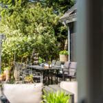 Terrasse mit Tisch, Stühlen und Pflanzen. Blick auf grüne Bäume und Hauswand.