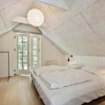 Schlafzimmer mit Dachschrägen, weißem Bett und Holzboden. Tür führt nach draußen.