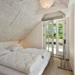 Schlafzimmer mit Doppelbett, weißen Wänden und Fenster zur Terrasse.