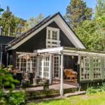 Schwarzes Holzhaus mit Terrasse und Glastür. Umgeben von Bäumen und Gras.