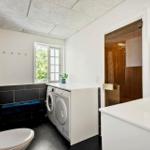 Badezimmer mit Waschmaschine, Dusche und Toilette. Fenster mit Blick auf Grün.