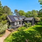 Schwarze Holzhütte mit Solaranlage, Terrasse und Garten in grüner Umgebung.