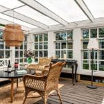 Glasdach über Terrasse mit Stühlen und Tisch. Holzdecke und Fenster sichtbar.