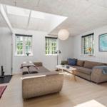 Wohnzimmer mit Kamin, Sofa und Fenstern. Holzboden und weiße Wände.