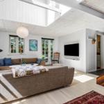 Wohnzimmer mit Sofa, Fernseher und Holzboden. Fenster und Türen führen nach draußen.