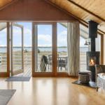 Wohnraum mit Kamin, Terrasse und Blick auf Wasser.
