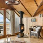 Wohnraum mit Kamin, Sessel und Terrasse mit Blick auf Wasser.