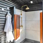 Außen-Dusche mit goldfarbenem Duschsystem und Holzklappe an schwarzer Holzwand.