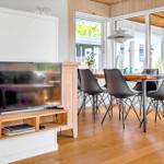 Ein Wohn- und Essbereich mit Fernseher, Holztisch und schwarzen Stühlen. Holzfußboden und große Fenster.