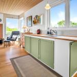 Küche mit grünen Schränken und Holzoberfläche. Blick auf Wohnzimmer mit Kamin und Sitzgelegenheiten.