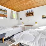 Zwei Betten mit weißen Bettdecken und gemusterten Laken. Holzdecke und Wandregal mit Dekorationsgegenständen.