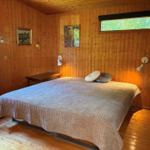 Schlafzimmer mit Holzwand, Bett, Fenster und Wandlampen.