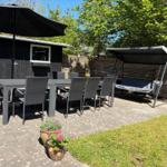 Terrasse mit Tisch, Stühlen, Sonnenschirm und Schaukel unter Bäumen.