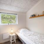 Ein Schlafzimmer mit Einzelbett, Fenster und Holzregal an der Wand.