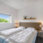 Schlafzimmer mit Doppelbett, Holzkopfteil, zwei Nachttischen und Fenster mit Blick auf Bäume.