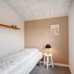 Ein Schlafzimmer mit Bett, Nachttisch und Wandbild. An der Wand hängt ein Bild. Ein Fenster ist sichtbar.