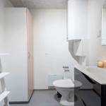 Badezimmer mit Toilette, Waschbecken und Regal. Weiße Wände und grauer Boden.