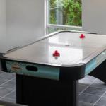 Ein Airhockey-Tisch mit roten Spielsteinen steht in einem Raum mit Fenstern und Fliesenboden.