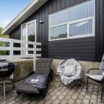Terrasse mit Liegestuhl, Grill und Sitzgelegenheiten vor schwarzem Holzhaus.