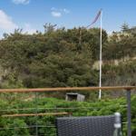 Terrasse mit Blick auf grüne Hänge und einen Mast mit rotem Band.